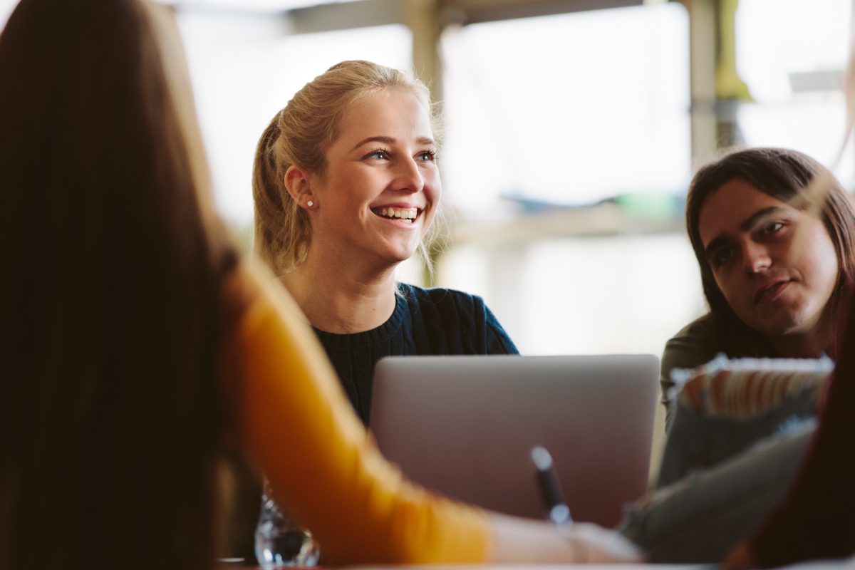 A woman smiles while sitting at a table with another person.