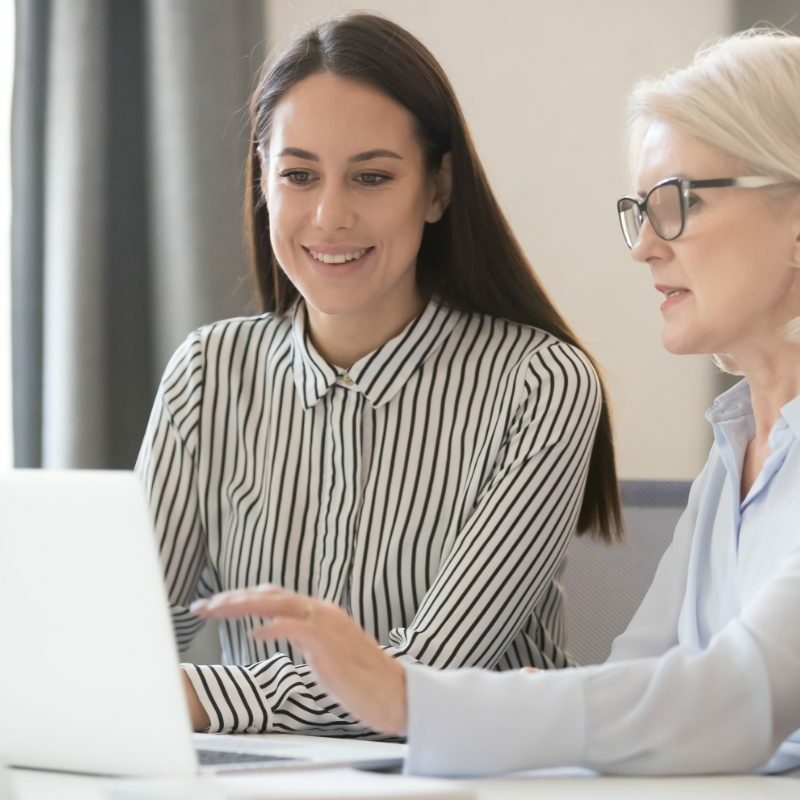 Two women sitting at a table looking at a laptop.